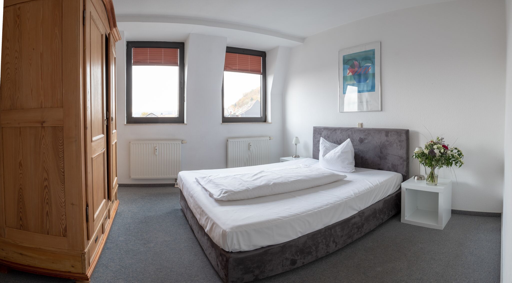 Schlafzimmer eines Apartments der City Residenz mit Doppelbett, Holzkleiderschrank und zwei Gaubenfenstern