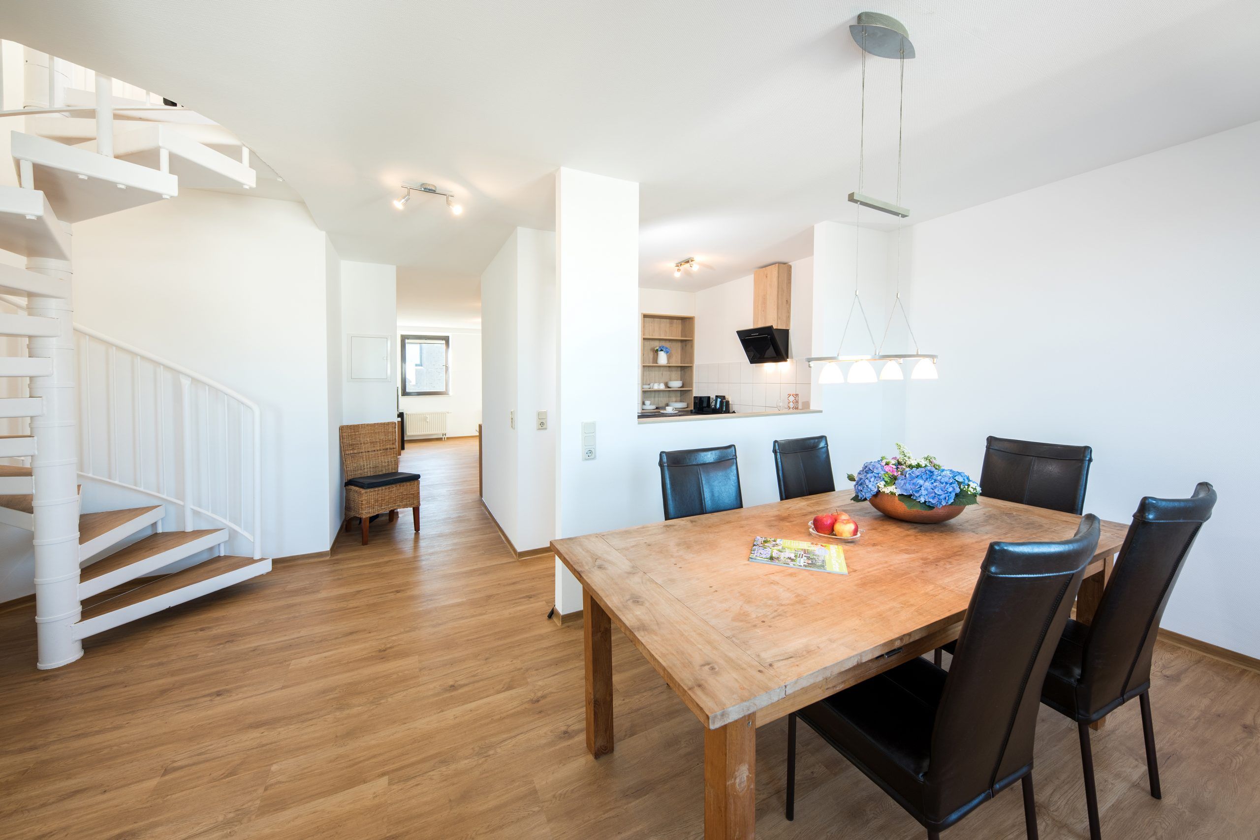 Essbereich einer Maisonette der City Residenz mit Holztisch, schwarzen Lederstühlen und weißer Wendeltreppe
