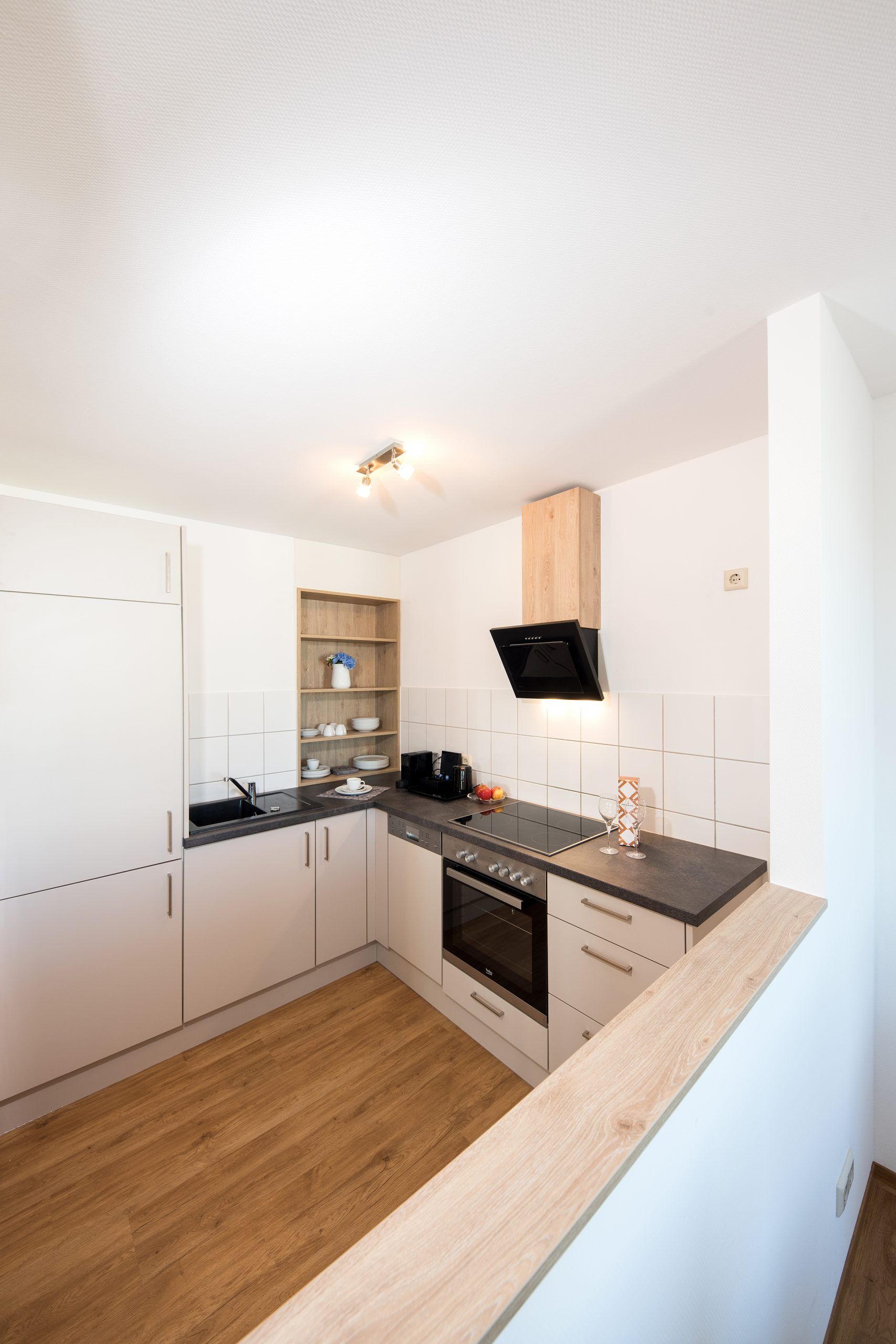 Einbauküche einer Maisonette der City Residenz mit Kochfeld, Backofen, Dunstabzug und offenem Holzregal