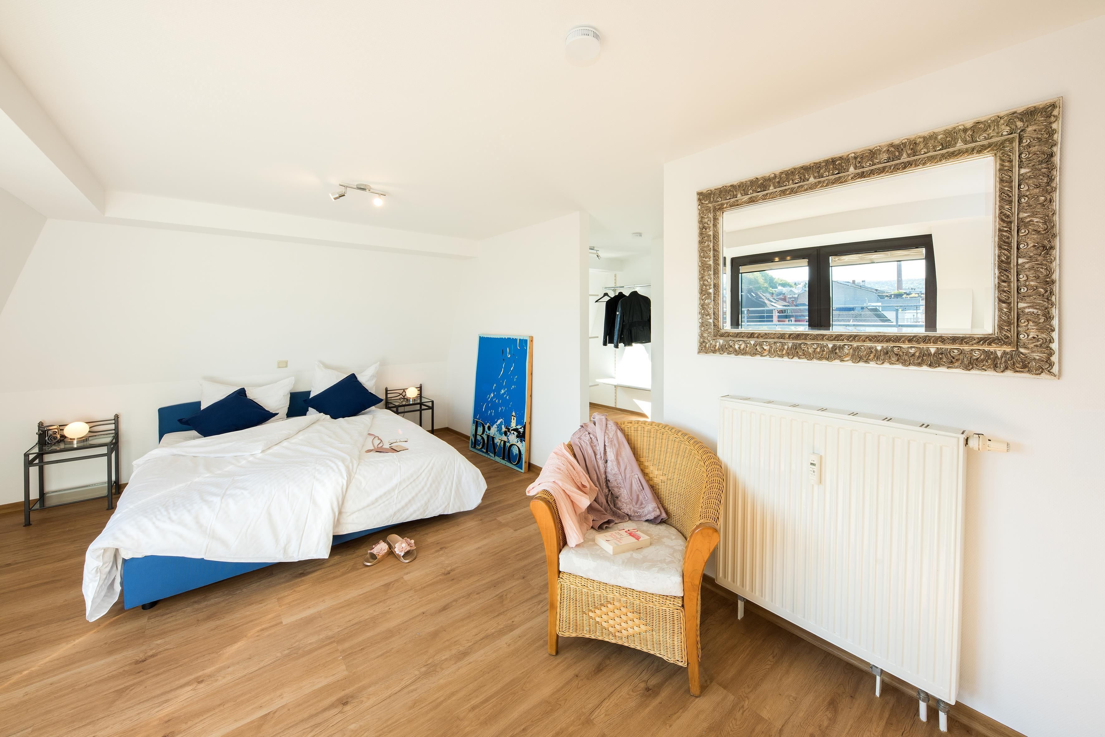 Schlafzimmer einer Maisonette der City Residenz mit blauem Doppelbett, Korbsessel und goldgerahmtem Spiegel