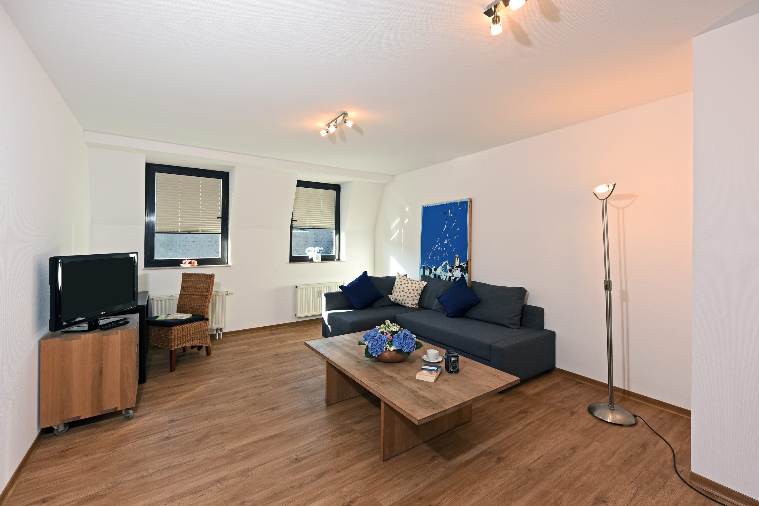 Wohnzimmer einer Maisonette der City Residenz mit Ecksofa, Holz-Couchtisch, Korbstuhl und Gaubenfenstern