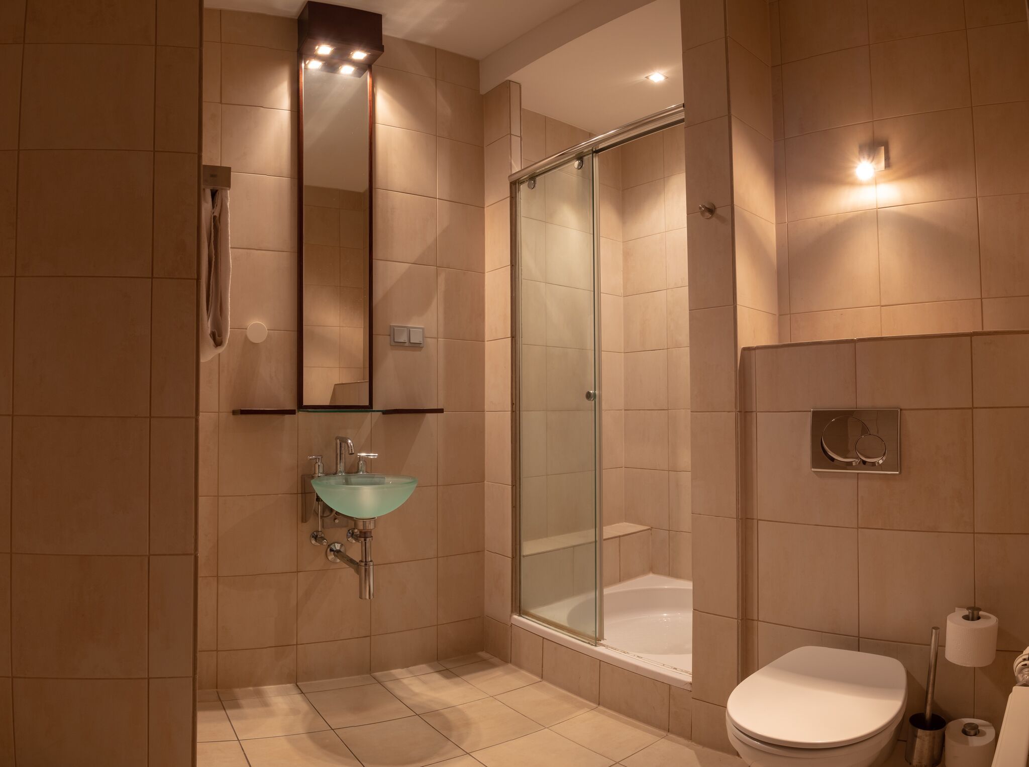 Duschbad eines Studios der City Residenz mit beigen Fliesen, Glaswaschbecken, Duschkabine und Wand-WC