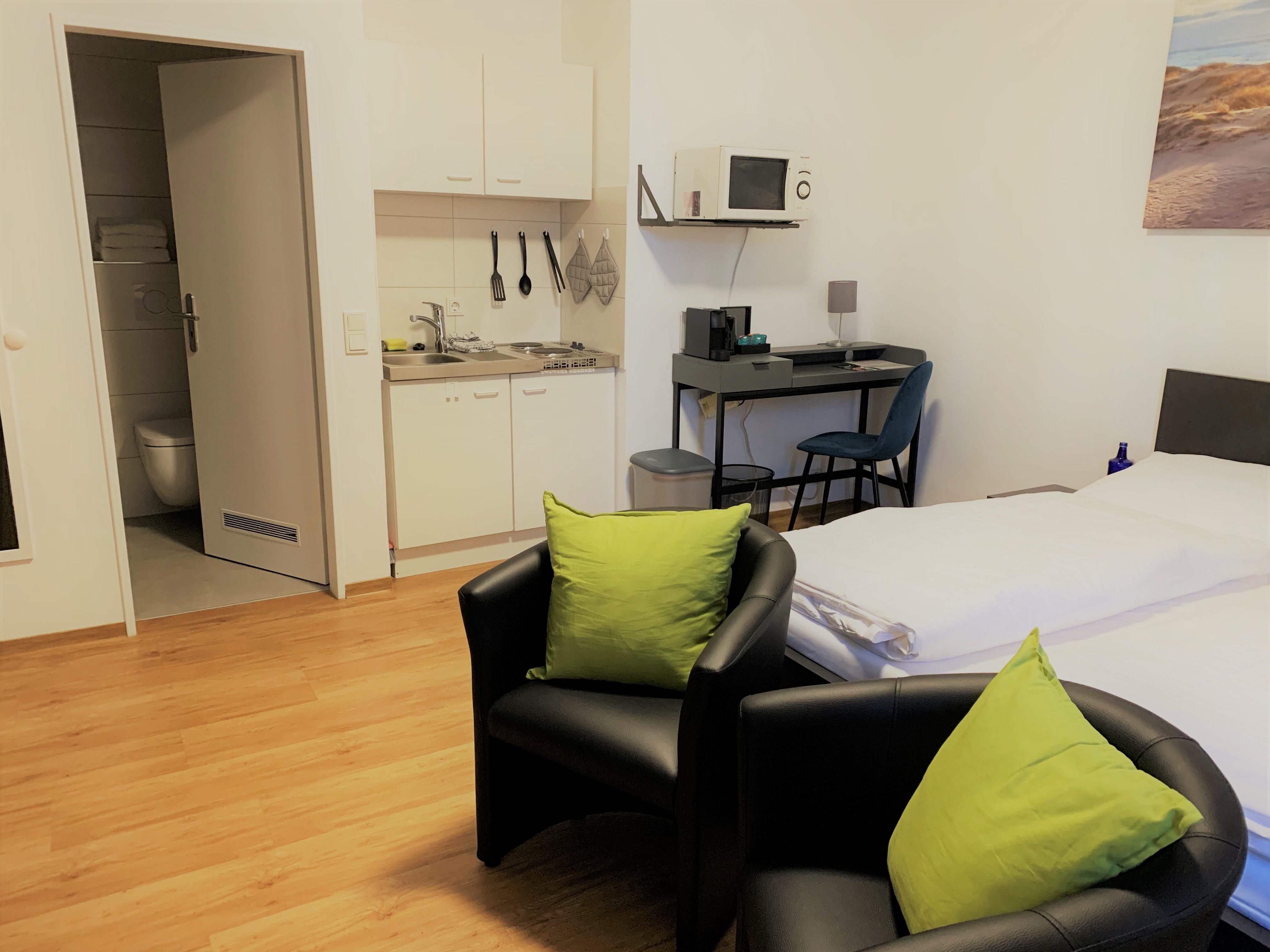 Studio der City Residenz mit Kitchenette, Mikrowelle, kleinem Schreibtisch, zwei schwarzen Sesseln mit grünen Kissen und Doppelbett