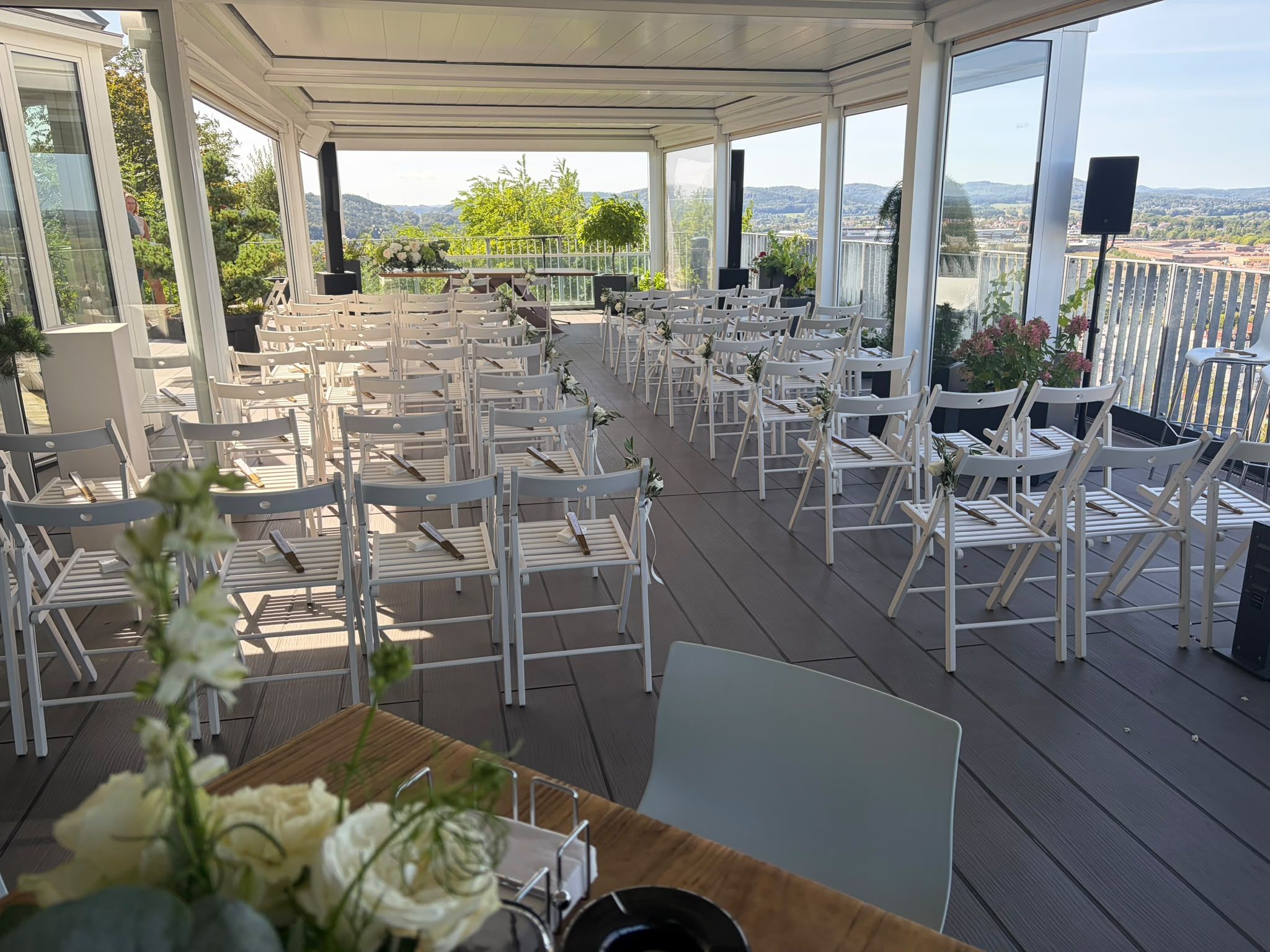 Weiße Stuhlreihen für eine freie Trauung auf der überdachten Terrasse, vorne Blumenschmuck, im Hintergrund der Blick über Homburg