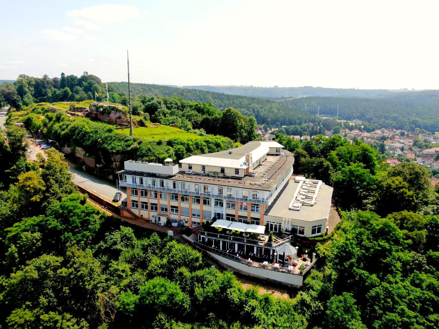 Luftbild des Hotels am bewaldeten Schlossberg mit der Restaurantterrasse, oberhalb die Mauerreste der Hohenburg, rechts die Dächer von Homburg