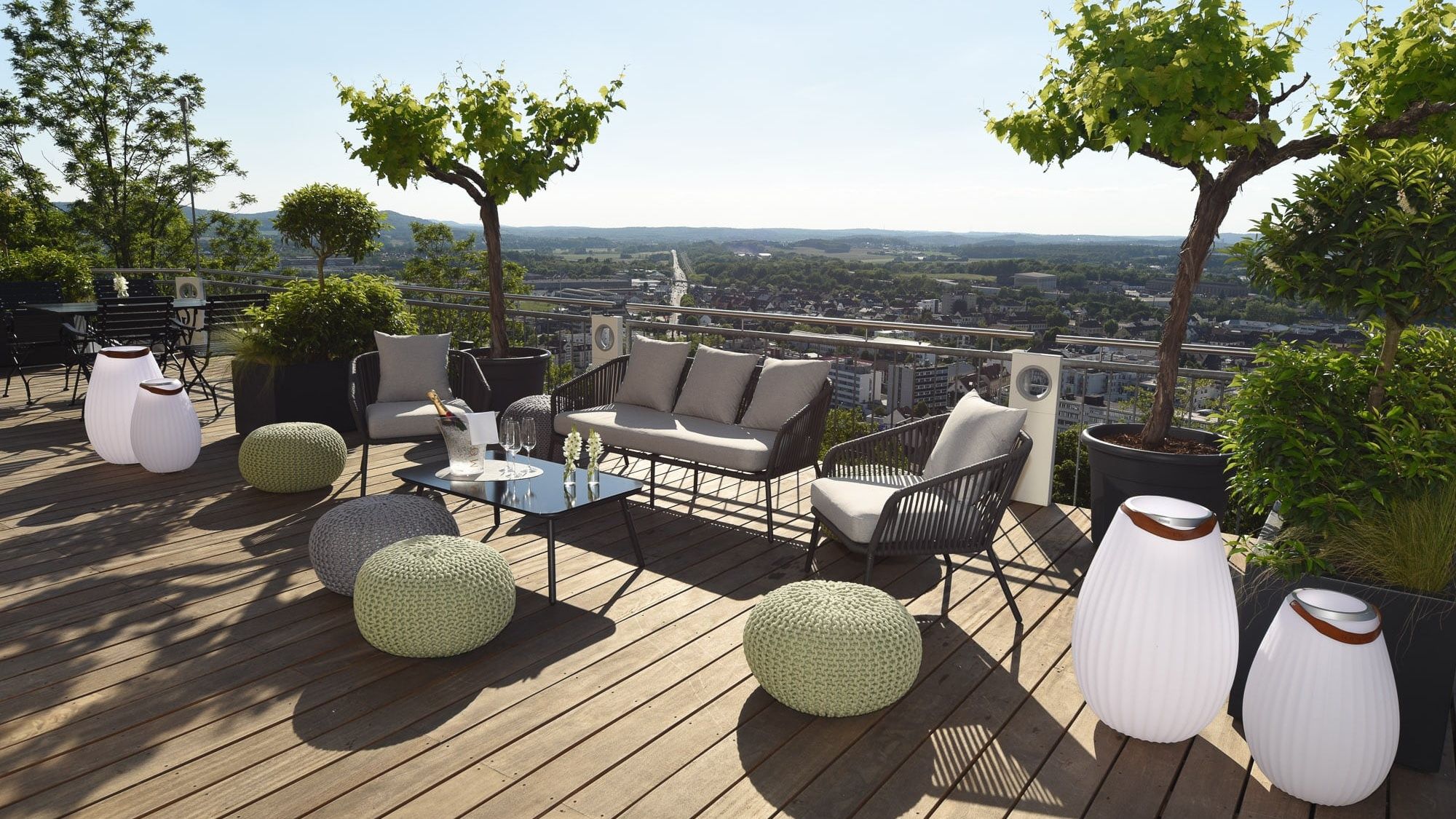 Lounge furniture, knitted poufs and lamp vases on the wooden terrace, with a view over the rooftops of Homburg