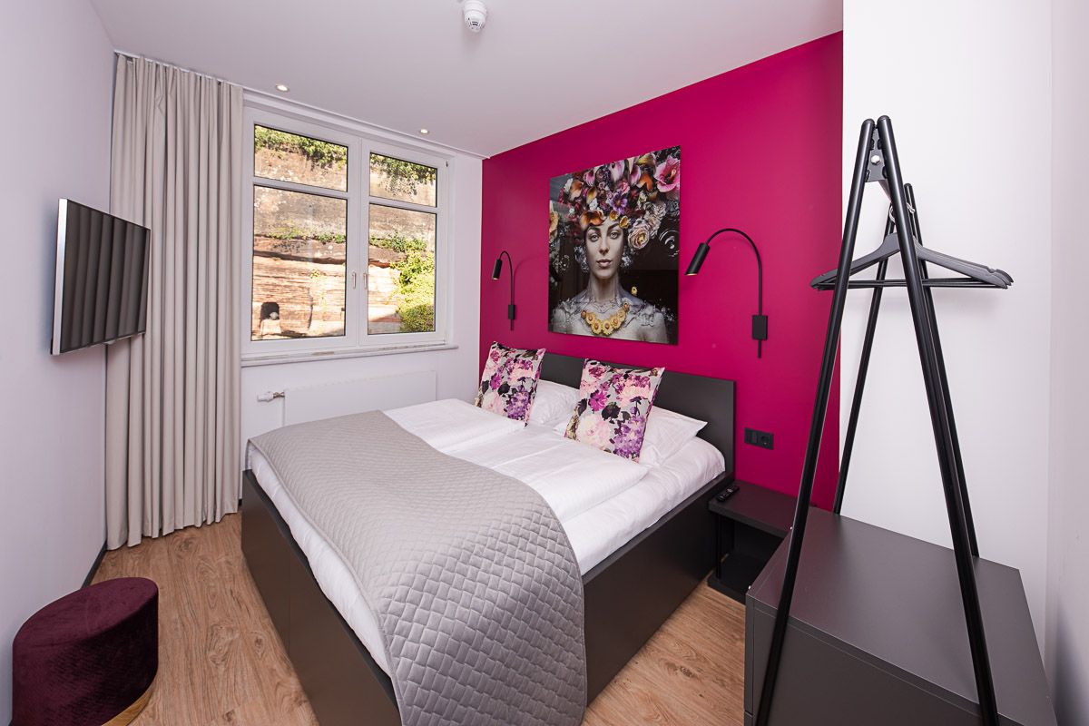 Comfort-Doppelzimmer mit pinkfarbener Wand, großem Porträt-Kunstdruck und Fenster mit Blick auf eine Sandsteinwand