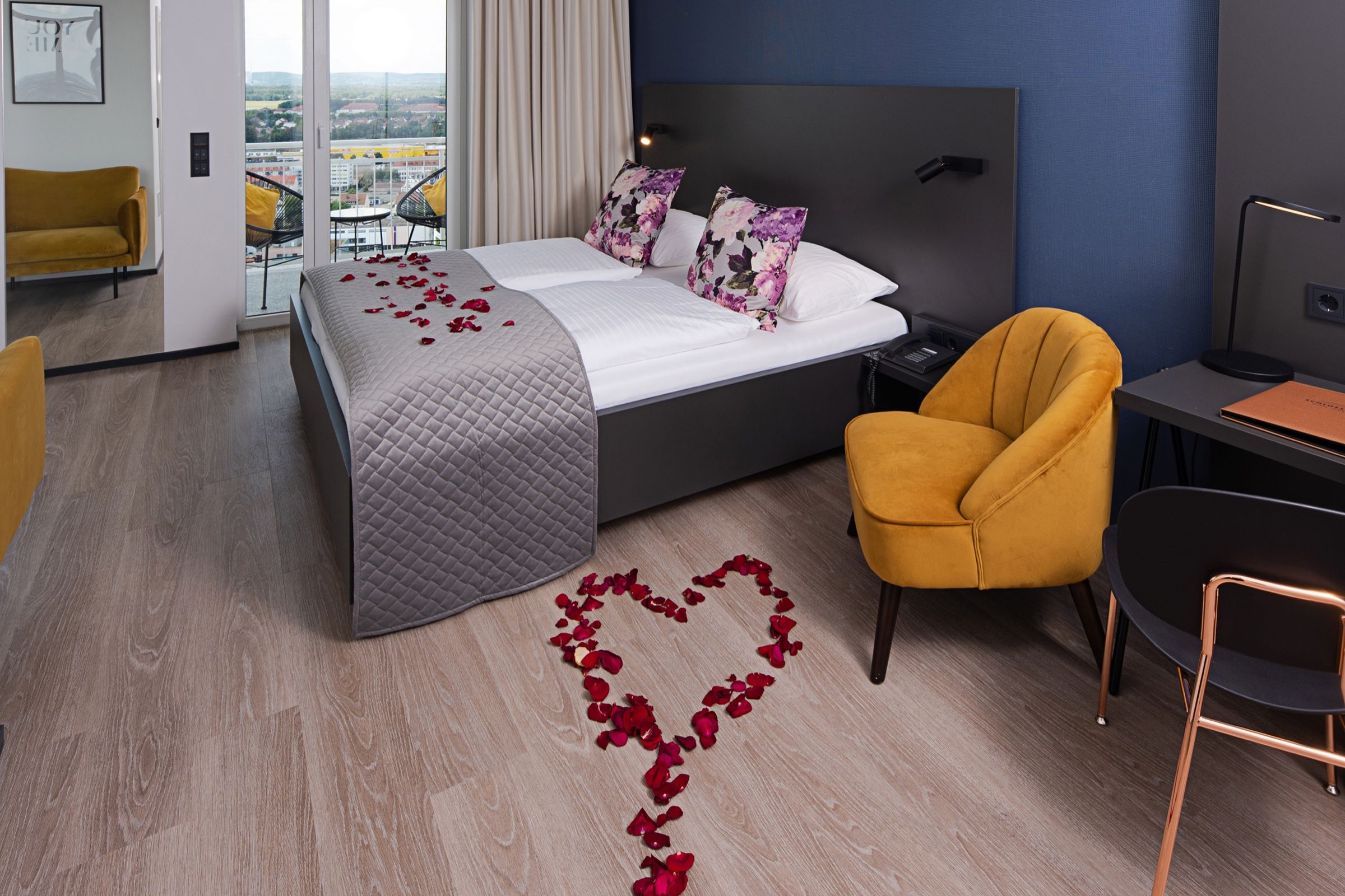 Doppelzimmer mit Rosenblättern auf dem Bett und einem Herz aus Blüten auf dem Boden, dahinter die Balkontür